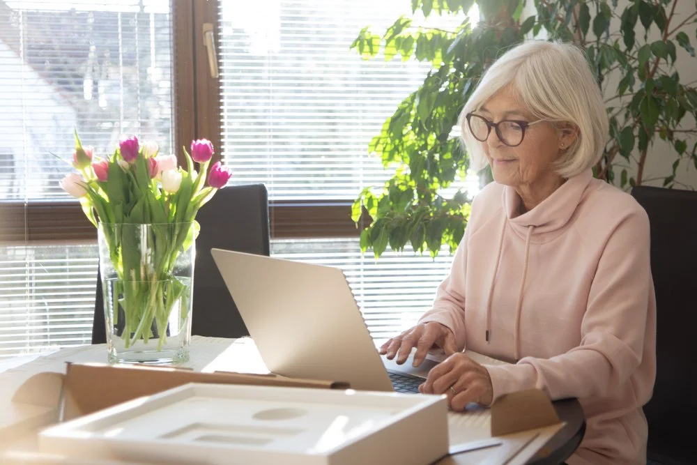 Excited senior woman setting up her new laptop computer, packaging still on the table